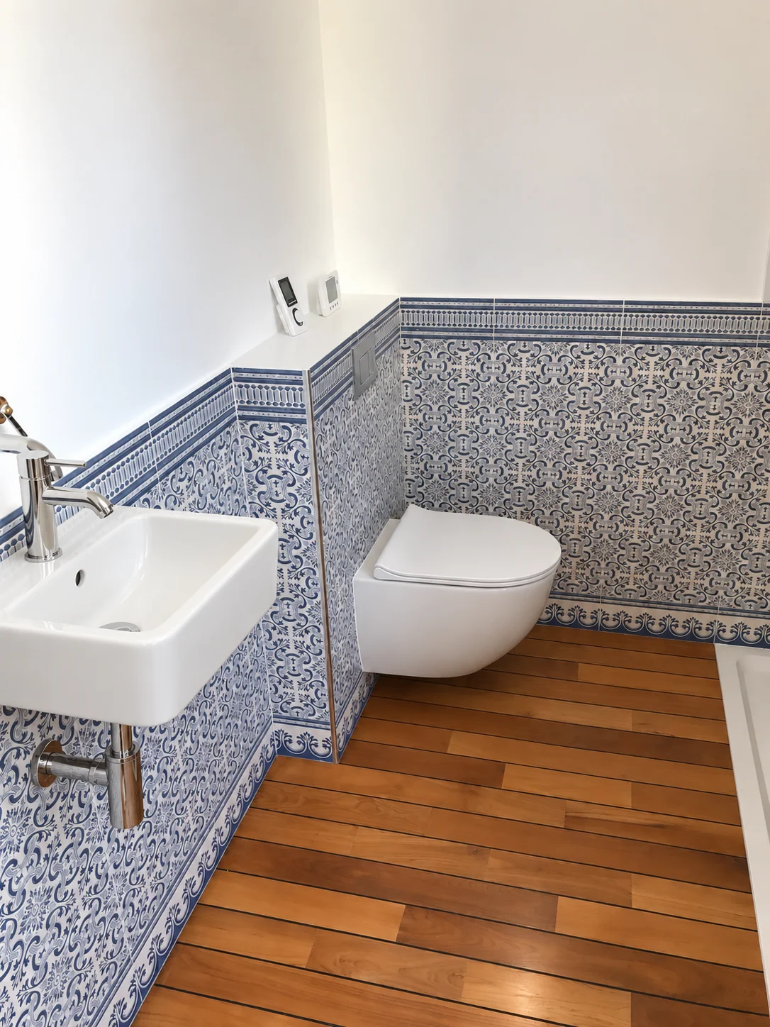 Lavabo et WC blancs avec carrelage bleu décoré et sol aspect bois.
