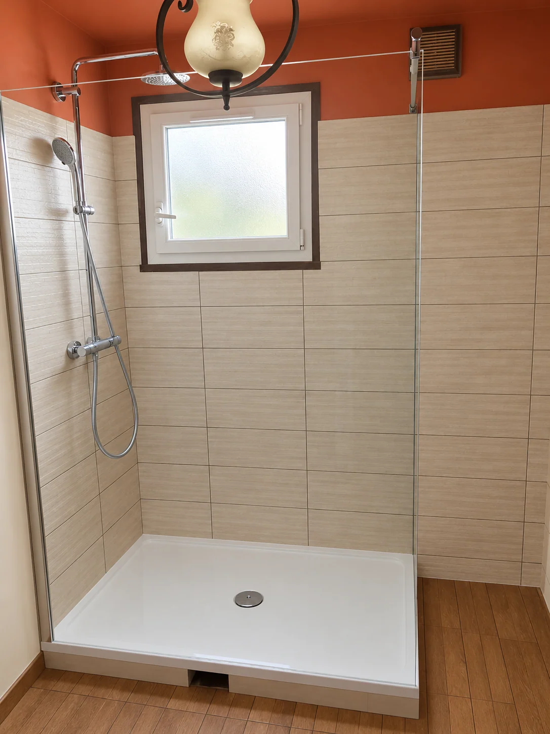 Douche avec receveur blanc, paroi vitrée, carrelage beige et mur haut orangé.