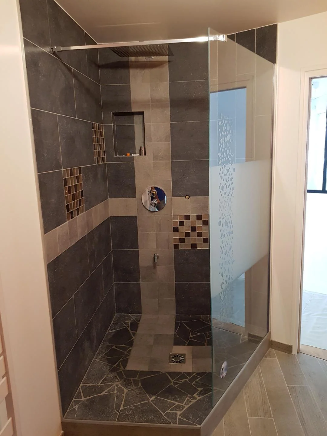Douche vitrée avec carrelage gris et inserts de mosaïque.