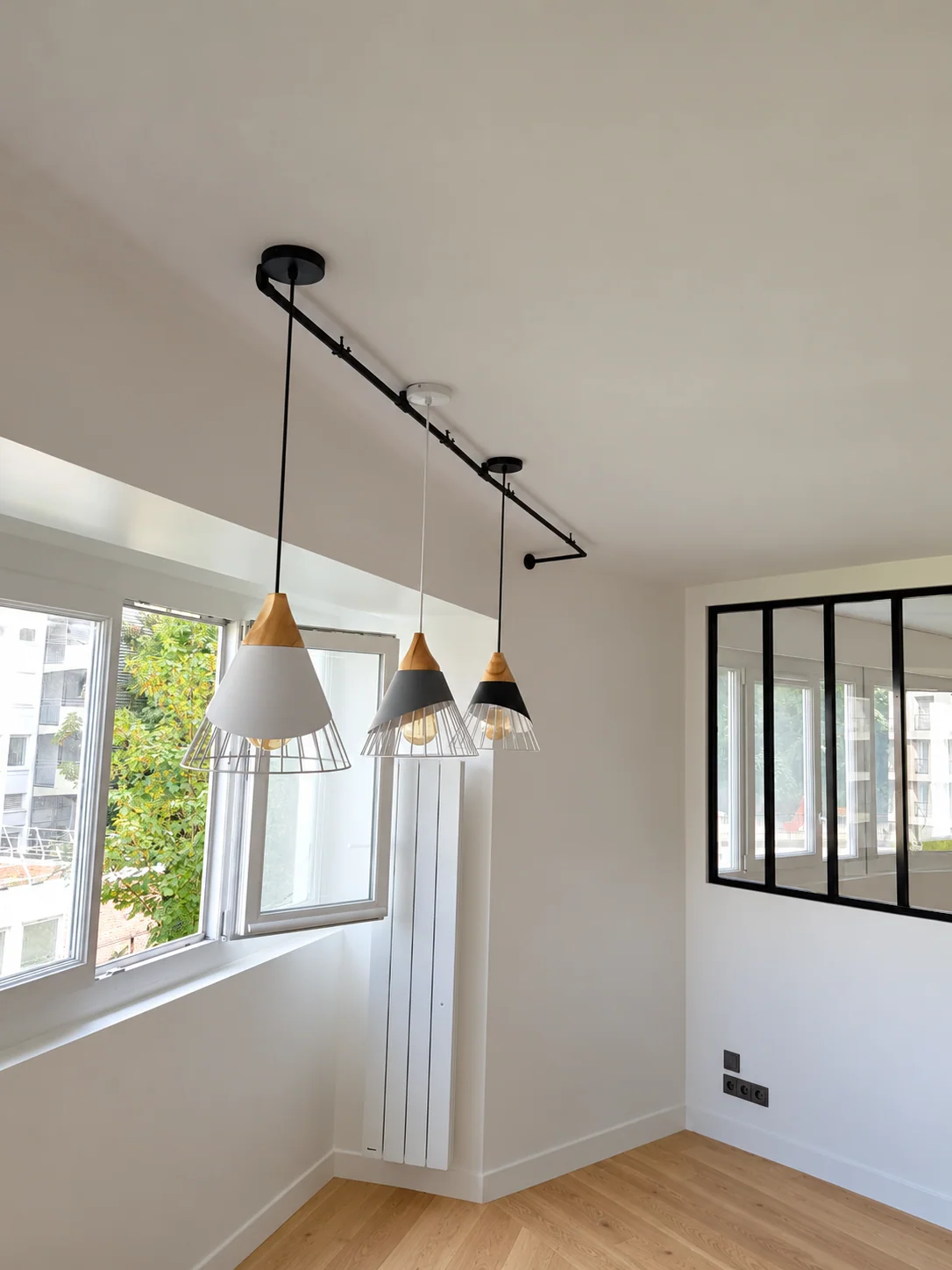 Pièce lumineuse avec suspensions, radiateur blanc et verrière noire.
