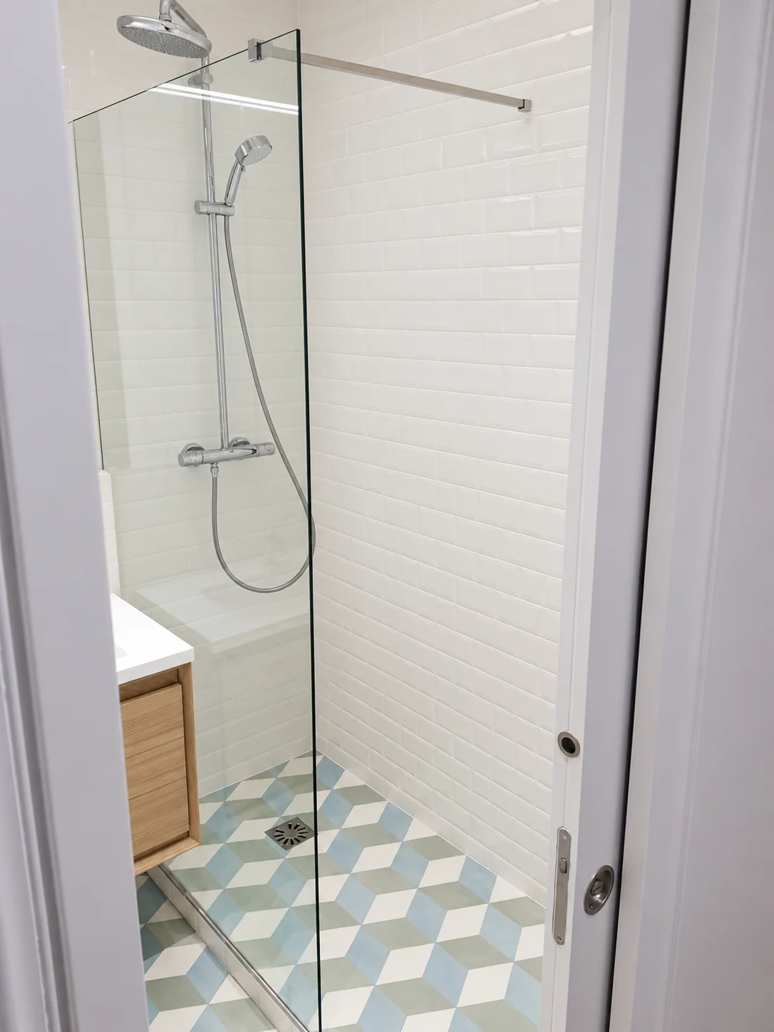 Douche vitrée avec faïence blanche et sol à motifs géométriques bleus et verts.