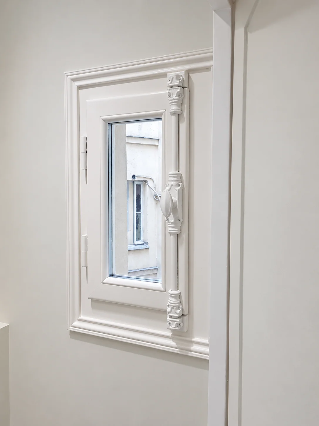 Petite fenêtre blanche avec crémone décorée.
